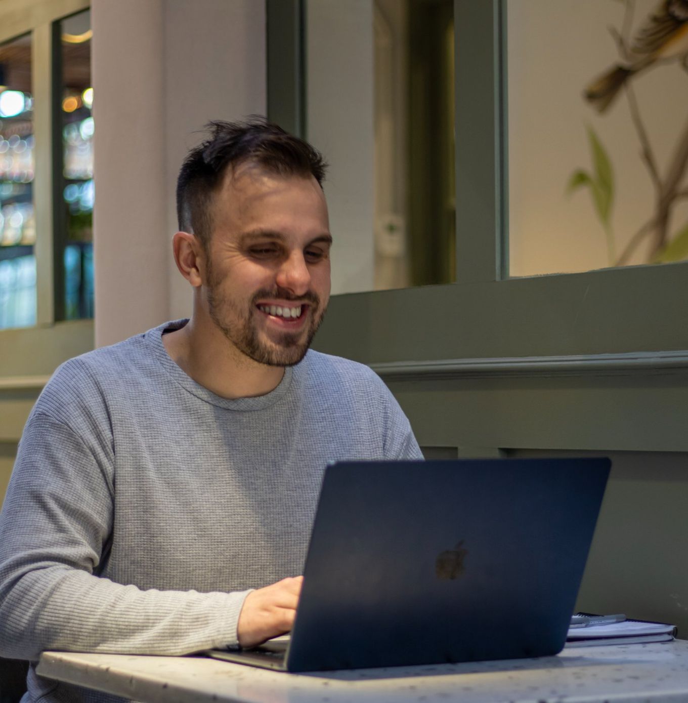 Alan Longo smiling while working at his laptop in a café